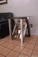 Side view of one end table showing glass top, metal legs, wood curved side panel, and decorative ladder metal center.