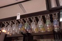Photo showing an array of vintage stemmed glasses hanging upside down on a rack with colored geometric patterns on the bowls including yellow, red, green, and blue.