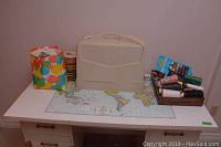 Photo showing all items on a white table with a world map mat; includes carrying case, ribbons, and sewing supplies in trays and bags.