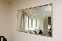 Framed rectangular mirror hanging on an off-white wall reflecting window and dining chairs.