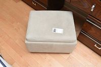 Small beige cushioned vanity stool on casters, placed on wooden floor beside wooden dresser.