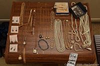 Full overview of costume jewellery lot arranged on wooden surface showing earrings, necklaces, brooch, bracelets, and pendants.