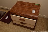 Single end table with wood grain top and beige drawer fronts, two drawers, gold-tone handles