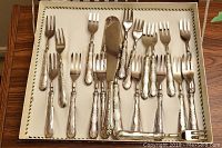 Full view of approximately 20-piece silver plated flatware set in a cream-lined box showing forks and serving knife with ornate handles.