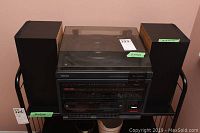 Front view of Toshiba stereo system with dust cover closed, showing unit between two wooden speakers on black metal shelf.