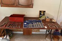 Overview of tools laid out on a wooden table, showing toolbox, wrenches, files, tin snips, and other hand tools.