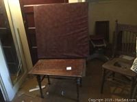 Folding card table with square leatherette-covered top, folded upright on wooden floor.