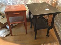 View of two vintage occasional tables side by side on wooden floor with wallpaper background, black table on right, ochre table on left
