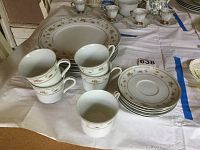 Set of stacked teacups, saucers, and dinner plates with floral and gold accents on white china