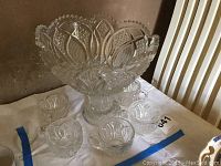 Full view of the footed crystal punch bowl with five matching crystal cups arranged in front on a white cloth.
