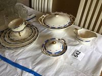Full view of entire 10-piece dinnerware set, showing decorative plates, cups, creamer, sugar bowl, and vegetable bowl with lid on a table.