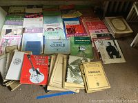 Wide view of sheet music laid out on floor showing variety of titles, including classical and guitar methods