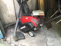 Red Snapper 2 cycle snow thrower, 19 inch LE model showing side view including chute and wheels, placed inside garage or shed.