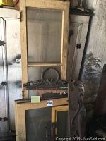 Full view of vintage wooden framed glass panels and carved trim pieces leaning against a wall in storage.