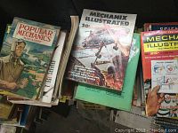 Initial photo showing stacks of Popular Mechanics, Mechanix Illustrated magazines with colorful 1950s and 1960s style covers including an airplane image and a man in a uniform.