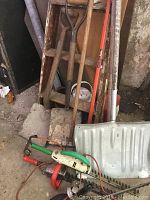 Vintage yard tools including shovels and electric trimmers leaning against shelving and wall in storage area