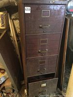 Front view of vintage filing cabinet with four file drawers and metal handles, surface rust and wear visible. Label holders on each drawer.