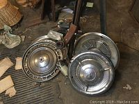 Four different Mopar hubcaps in a pile with chrome trim and VW jack on floor