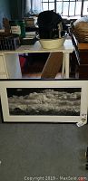 Framed landscape photo lithograph attributed to Ansel Adams, leaning against furniture and window in room.