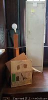 Overall view of wooden floor lamp standing behind cardboard box containing vaporizer box and next to tall metal storage locker