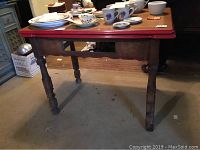 Wooden table legs and side profile showing aged finish and turned legs, with red enamel top surface visible from the side.