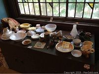 Wide view of tole black table holding over 40 pieces including china, pottery, glassware near a window with leaded panes