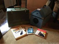 Photo of two vintage cardboard cat carriers, three books about cats or pets, and a self-grooming kitty comb in package.