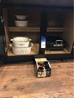 Photo of Corningware casseroles, mixing bowls, and roasting pan inside cabinet, with boxed butter warmers on floor of cabinet.