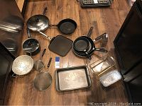 Overview photo showing various pots, pans, strainers, baking sheets, and kitchen tools laid on floor