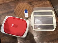 Two white Tupperware containers stacked with red lids, round wooden tray on the side, and four clear rectangular containers with beige handles stacked