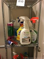 Cleaning supplies arranged on metal shelving showing multiple spray bottles, ammonium container, and cleaning powder canister.