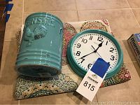 Ceramic utensil caddy, round wall clock placed on colorful folded fabric with circular patterns on a tiled surface.