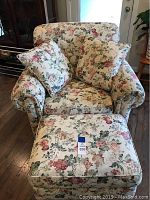 Front view of the floral fabric oversized chair with matching ottoman and cushions, set on a wooden floor.
