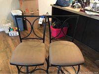 Pair of metal swivel barstools with tan fabric seats and circular backrest design.