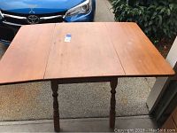 Top view of drop leaf table showing one leaf dropped and the other leaf extended, with a sticker on the center section.