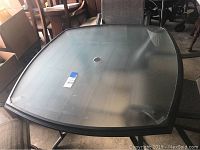 Square glass patio table viewed from above showing glass top and black metal frame.