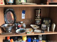 Wide view of the shelf with all items in lot including silver plate bowl, tray, tea tins, cocktail forks, shaker, cups and decorative bowl