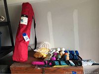 Various sporting goods including weighted gloves, wrist and ankle weights, dumbbells, a red folding chair in carry bag, and accessories laid on wooden surface