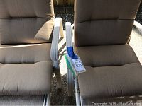 Close-up of two beige cushioned outdoor loungers side by side showing armrests and cushions.