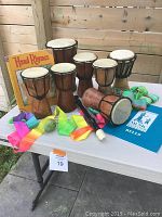 View showing eight wooden kid's drums, colorful dance ribbons, egg shaker, black recorder, and two children's music books on a table.