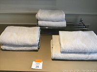 Photo shows six white towels in different sizes and textures grouped on a flat surface with a chrome wall mounted towel rack positioned behind them.