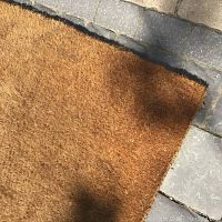 Close-up of the natural fiber coir door mat showing its thickness and weave, on stone floor.