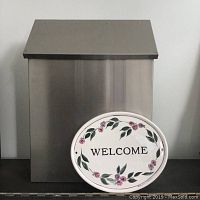 Stainless steel mailbox with oval welcome plaque in front, showing size and condition.