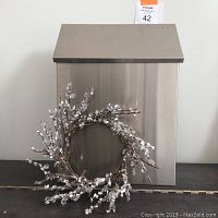 Front view of stainless steel mailbox with decorative wreath placed in front of it.