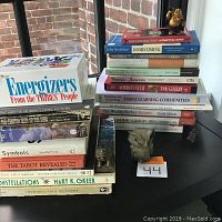 Photo of all stacked books showing variety of self-help, therapy, tarot, and esoteric topics with a small statue next to the pile.