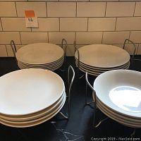 View of assorted white ceramic plates stacked in metal plate holders, including dinner, side, and pasta plates.