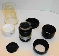 Nikon Nikkor-Q 135mm f/3.5 lens with various accessories including lens caps, lens hood, mounting ring, and clear plastic case.