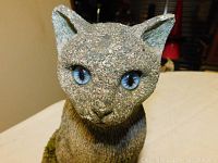 Close-up front view of cement cat statue showing detailed rough texture and blue eyes