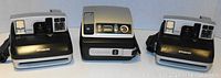 Front view of 3 Polaroid instant cameras: two OneStep (left and right) and one Spectra (center)