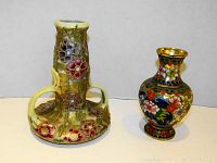 Photo showing both floral vases: a ceramic vase with raised flower designs and two handles, and a smaller cloisonné-style vase with colorful floral patterns.